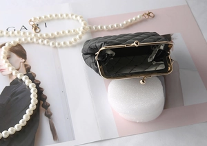 Detail view of black quilted faux leather handbag with pearl chain and gold metal clasp