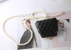 Detail of black quilted mini bag featuring golden kiss-lock and elegant pearl chain strap