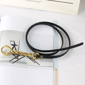 Close-up of a slim black leather belt with a luxury twisted gold metal buckle on a magazine