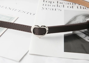 Dettaglio di cintura sottile in pelle marrone scuro con fibbia a cuore in argento lucido