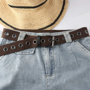 Brauner Canvas-Gürtel mit Metallösen auf hellblauer Jeans mit einem Sommerhut