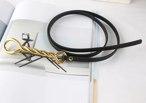 Detail of slim black leather belt with a twisted gold metal buckle on a desk