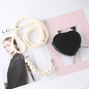Detail of heart-shaped black mini bag with elegant faux pearl strap on fashion magazine