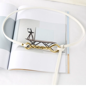 Detail of white thin belt featuring a twisted gold buckle on a stylish magazine background