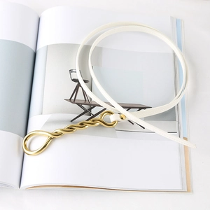 Detail view of a white leather thin belt with a gold rope textured metal buckle on a magazine