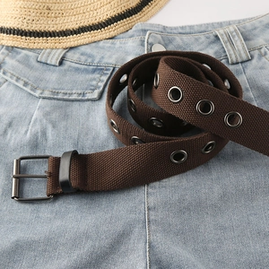 Brauner Leinwandgürtel mit Metallösen und schwarzer Dornschließe auf blauer Jeans