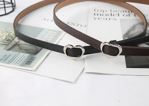 Dettaglio di cinture sottili in pelle con fibbie a cuore argento in nero e marrone