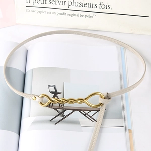 Detail of slim beige faux leather belt with a decorative gold twisted metal buckle on a magazine