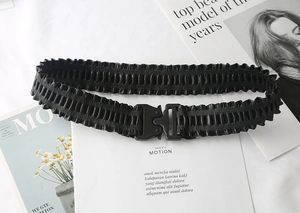Detail of black pleated elastic waist belt with textured metal tactical buckle closure