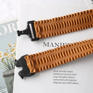Close-up of brown pleated leather belt with elastic accordion folds and black plastic buckle