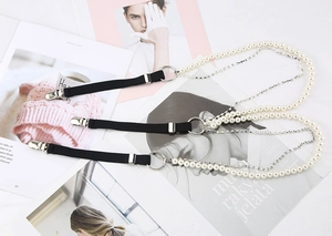 Dettaglio di una clip chic con perle bianche, strass e fettuccia elastica nera per abiti
