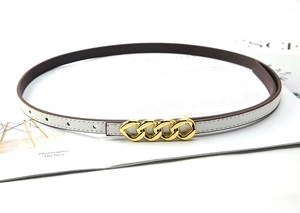 Detail view of slim white leather belt with gold chain buckle on a fashion magazine