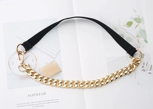 Close-up of gold chunky chain with black fabric strap and round metal snap hooks