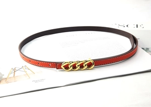 Detail of red lychee grain leather belt with a triple-link gold chain buckle on a magazine