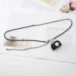 Close-up of a silver chain belt with black leather weave and a pearl mini bag charm