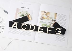 Detail of black elastic belt featuring decorative gold metal letters and buckle on a magazine