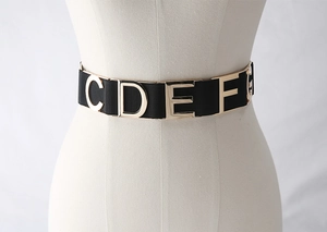 Close-up of black elastic waist belt with gold metal letters on a dress mannequin