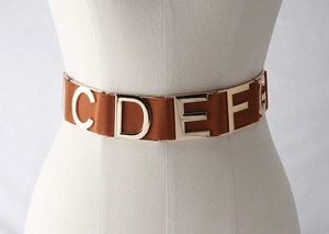 Macro detail of elastic corset belt featuring polished gold metal letters on brown strap