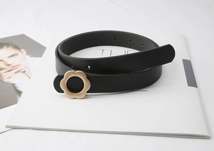 Détail de l'élégante boucle fleur dorée sur une ceinture fine en cuir noir minimaliste