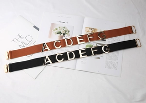 Detail of elastic waist belts in black and brown with gold metal letter decorations