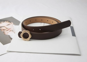 Détail d'une fine ceinture en cuir marron foncé avec boucle en métal doré en forme de fleur