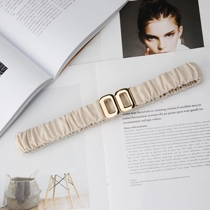 Detail of beige elastic waist belt featuring a gold square double buckle on white background