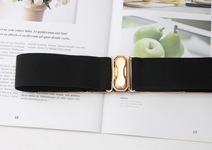 Detail of black elastic belt featuring a golden octagonal buckle on a fashion magazine
