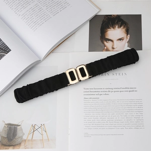Black elastic waist belt with gold double-ring metal buckle on minimalist background