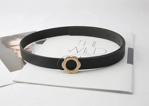 Détail d'une ceinture fine en cuir noir avec une boucle dorée en forme de fleur élégante