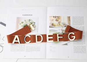Close-up of caramel elastic belt featuring gold metal letters on a stylish fashion magazine