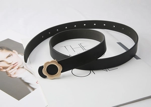 Détail d'une fine ceinture en cuir noir avec boucle dorée en forme de fleur sur magazine