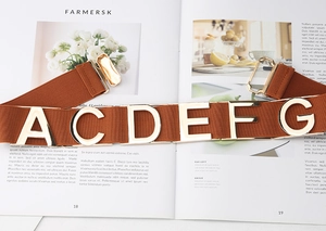 Close-up of caramel elastic belt with gold metal letters and hook buckle on a magazine