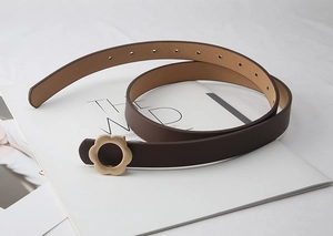Détail d'une fine ceinture en cuir marron foncé avec boucle fleur dorée sur un magazine