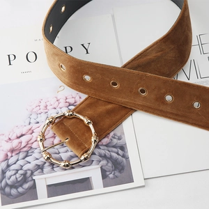 Detail of a brown velvet belt with a gold bamboo-textured round buckle and eyelets