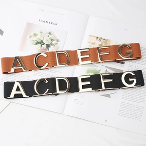 Elastic waist belts with gold metal letter buckles in black and brown over a fashion magazine