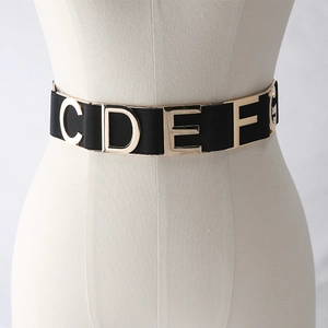 Women's wide elastic black waist belt with gold metal letters on a beige mannequin
