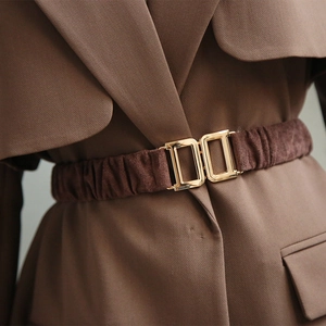 Detail of a brown elastic waist belt with a golden metallic buckle on a matching blazer