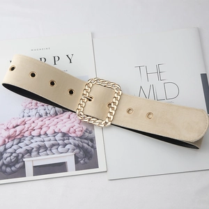 Détail d'une large ceinture beige avec une grande boucle carrée dorée à maillons