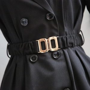 Close-up of a wide elastic waist belt with interlocking gold buckle on a black blazer