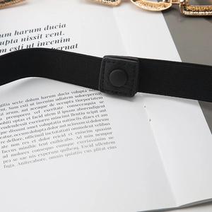 Λεπτομέρεια μαύρης ελαστικής ζώνης με χρυσή αλυσίδα και κουμπί με ανάγλυφη υφή