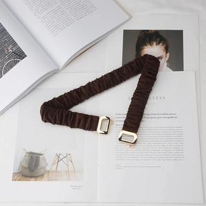 Close-up of dark brown elastic waist belt with a gold rectangular metal buckle on books