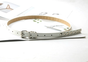 Detailed macro view of white slim leather belt with silver pyramid studs and metal buckle