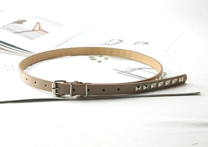 Close-up of slim taupe waist belt with silver square rivets on a fashion magazine