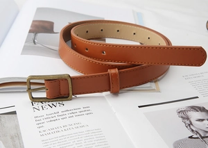 Detail of a brown leather belt with vintage bronze buckle on a fashion magazine