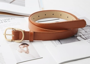 Close-up of brown leather belt with gold D-ring buckle on a fashion magazine