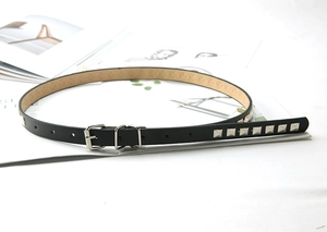 Close-up of a black skinny leather belt featuring square silver metal studs and pin buckle