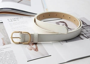 Close-up of white leather belt with matte gold oval buckle and woven metal details