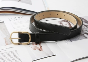 Detail of minimalist black faux leather belt with a matte gold oval buckle on fashion magazine
