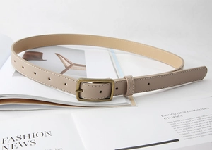 Detail of a beige leather belt with white stitching and antique bronze buckle on a magazine