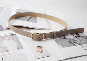 Detail shot of a slim taupe leather vintage belt with an oval matte gold buckle